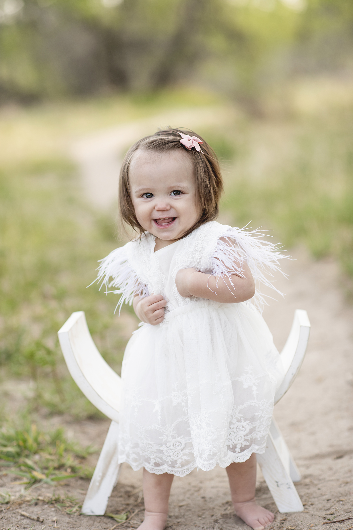 One Year Old Baby girl standing in nature with a white dress on smiling