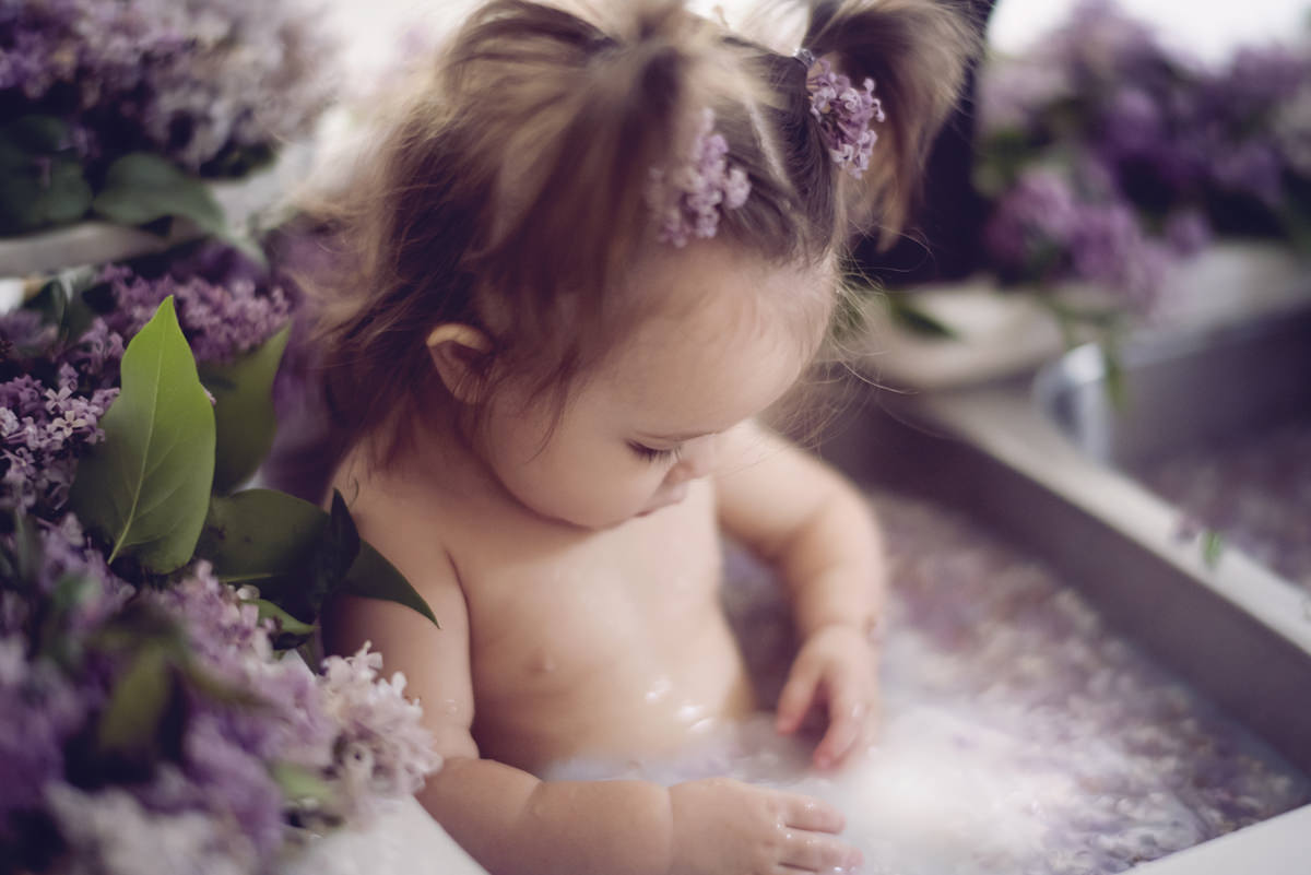 one year old baby with pigtails in a kitchen sink full of milk and surrounded by fresh lilacs