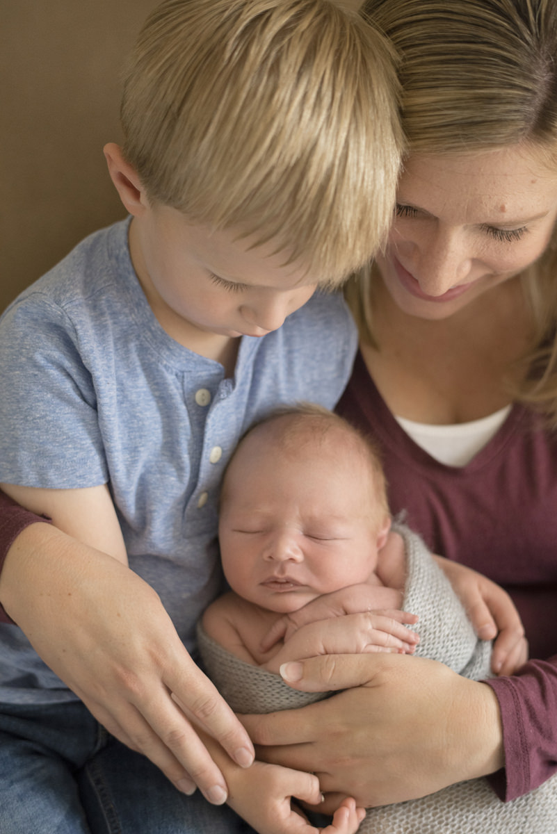 Newborn baby in a gray crocheted wrap held by big brother and mom