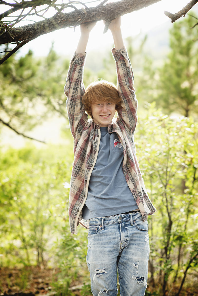 teen boy with red hair dressed in a plaid shirt hanging from a branch
