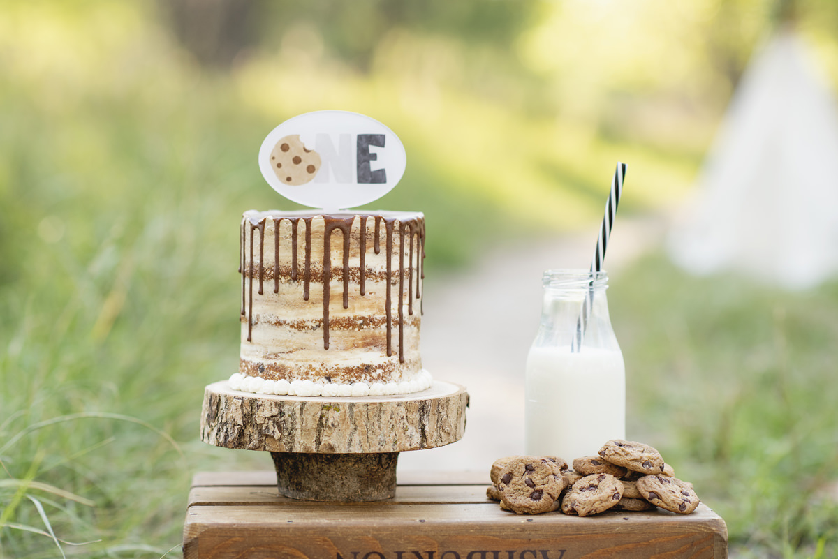 Milk and Cookies Next to a naked frosting cake withe chocolate drizzle and a first birthday cake topper
