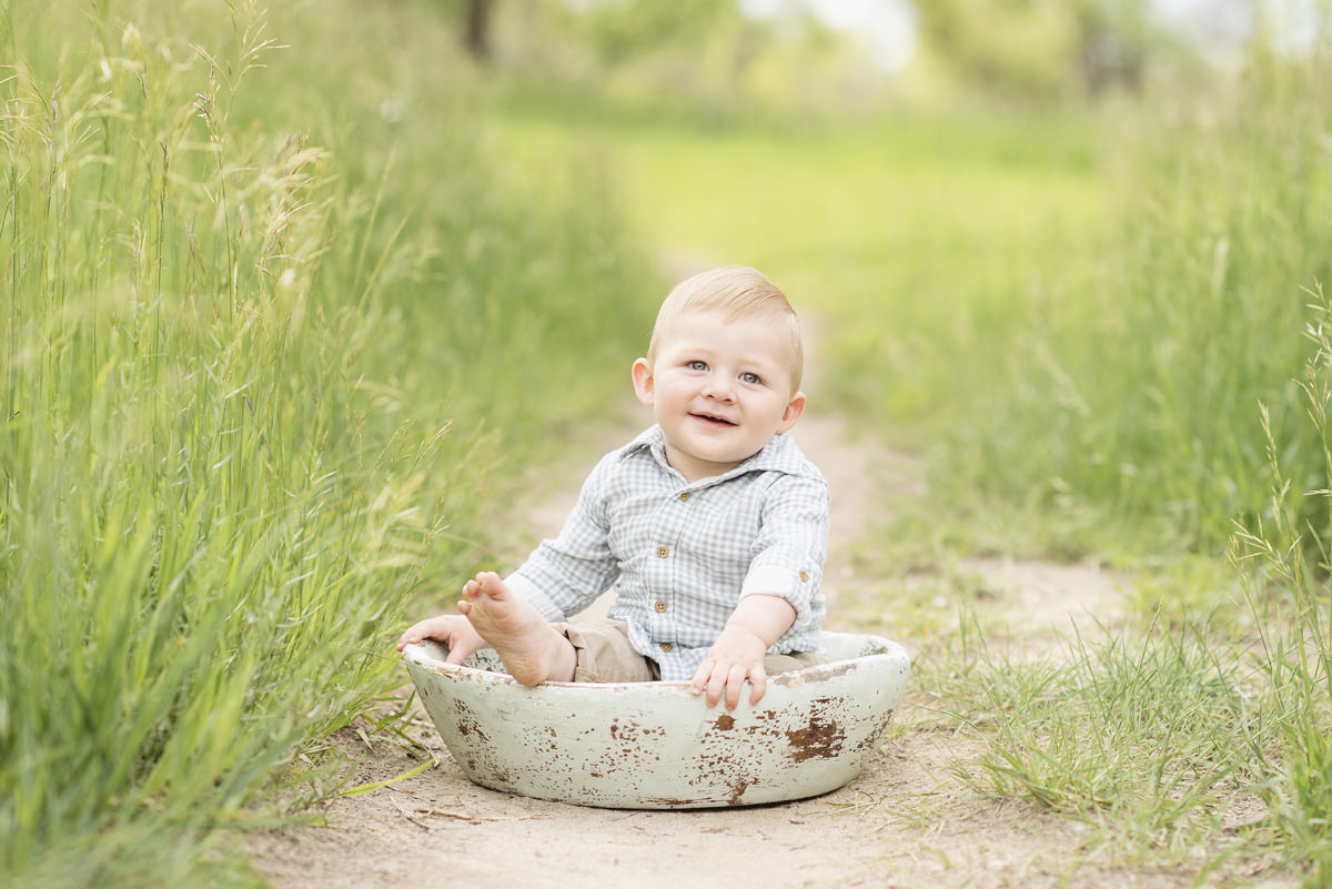 baby sitting in a green large wooden bowl on a dirt path with long grass