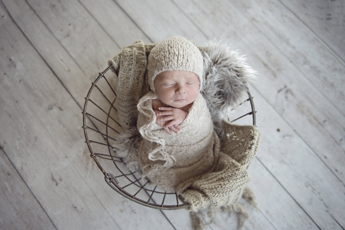 newborn baby in wire basket wrapped in neutral colors taken by a professional newborn photographer in Colorado