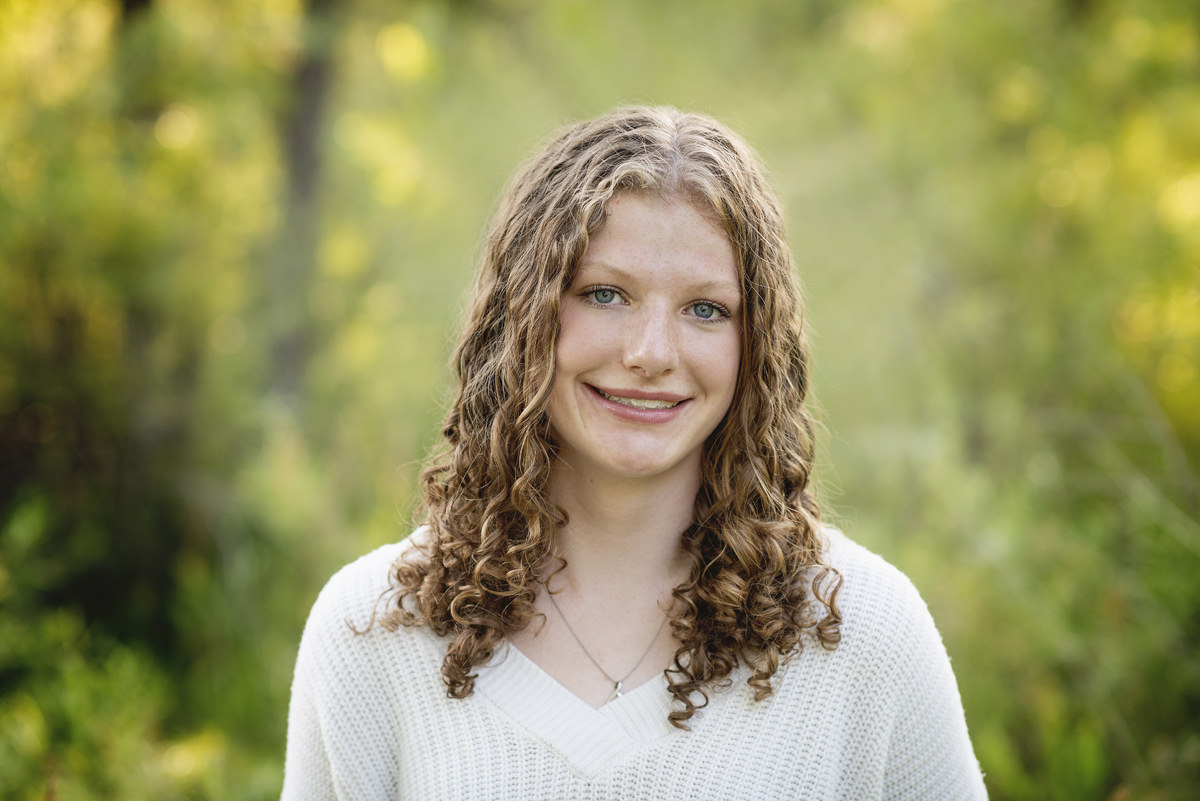 High school senior girl headshot in nature with curly hair, wearing a white shirt
