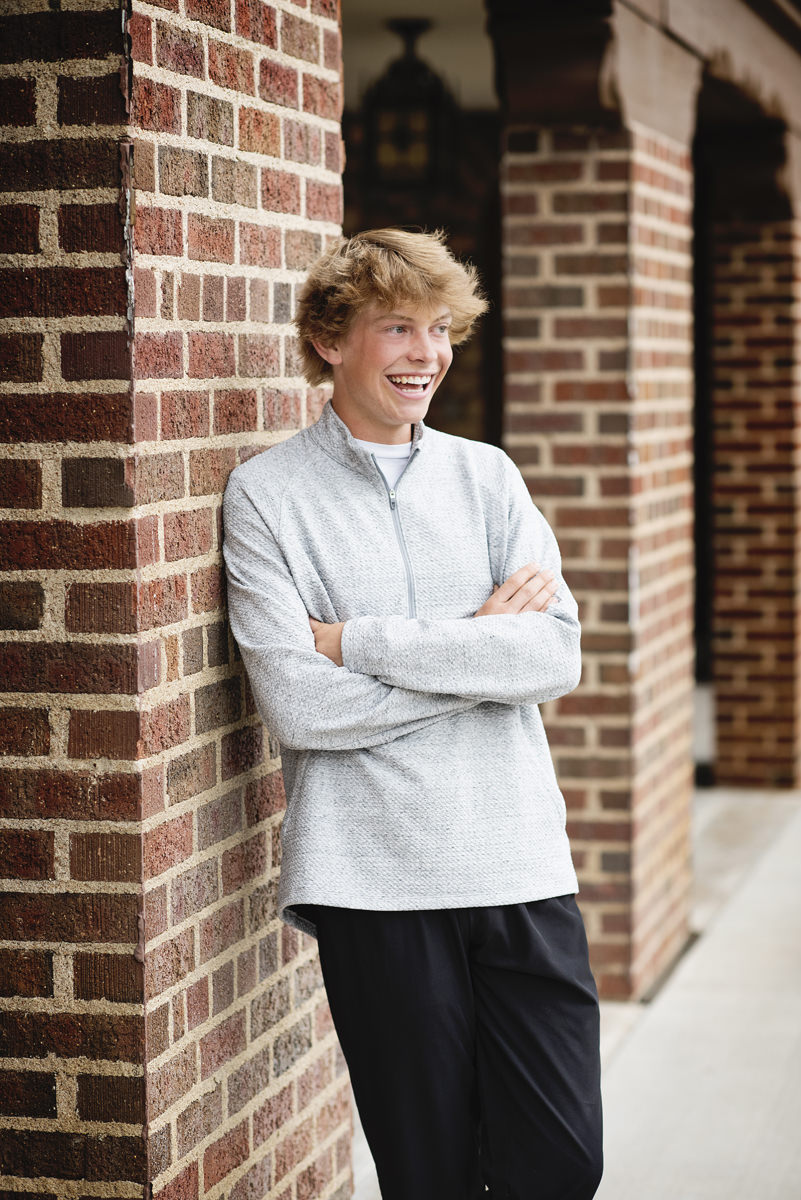 Senior Pictures Guy against brick columns wearing a gray shirt with black pants