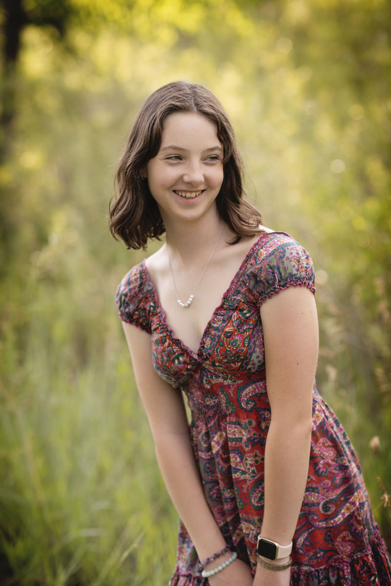High school senior girl pose in dress lifestyle looking away from camera with her hands on her thigh and smiling