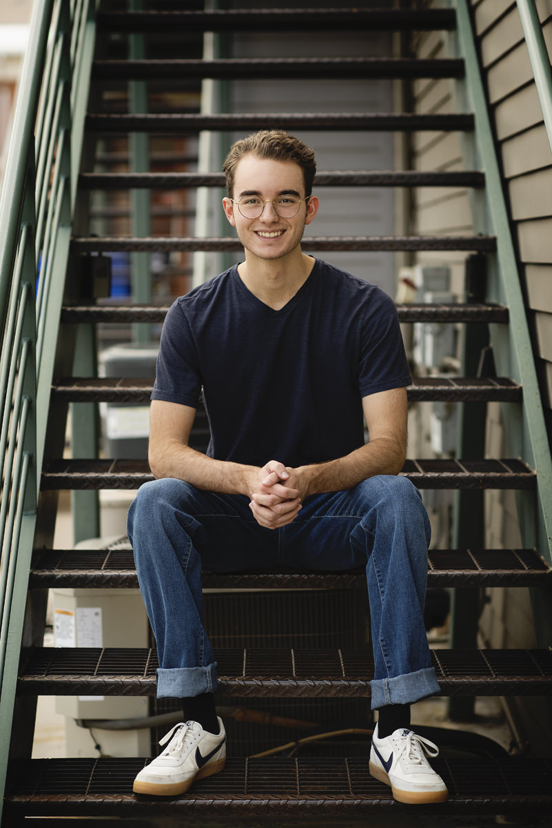 high school senior boy sitting on metal steps for his senior pictures