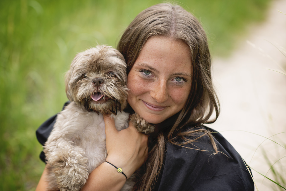 High school senior girl hugging small dog in her senior pictures wearing a black shirt outdoors