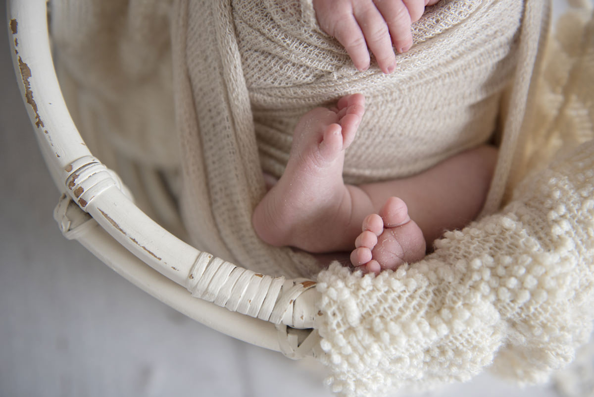 Newborn baby feet wrapped up like a pretzel comfortably in a creme colored wooden basket