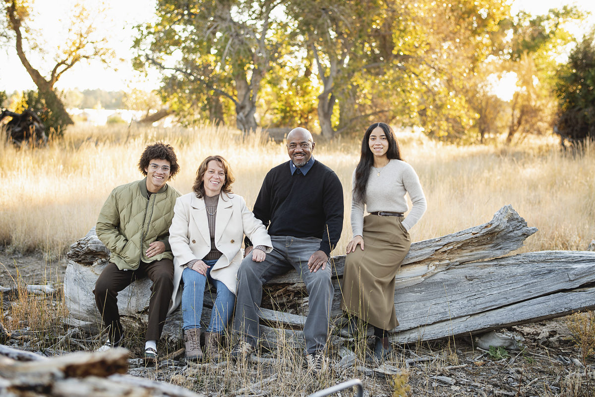 Mixed family pictures sitting on a fallen log with adult children