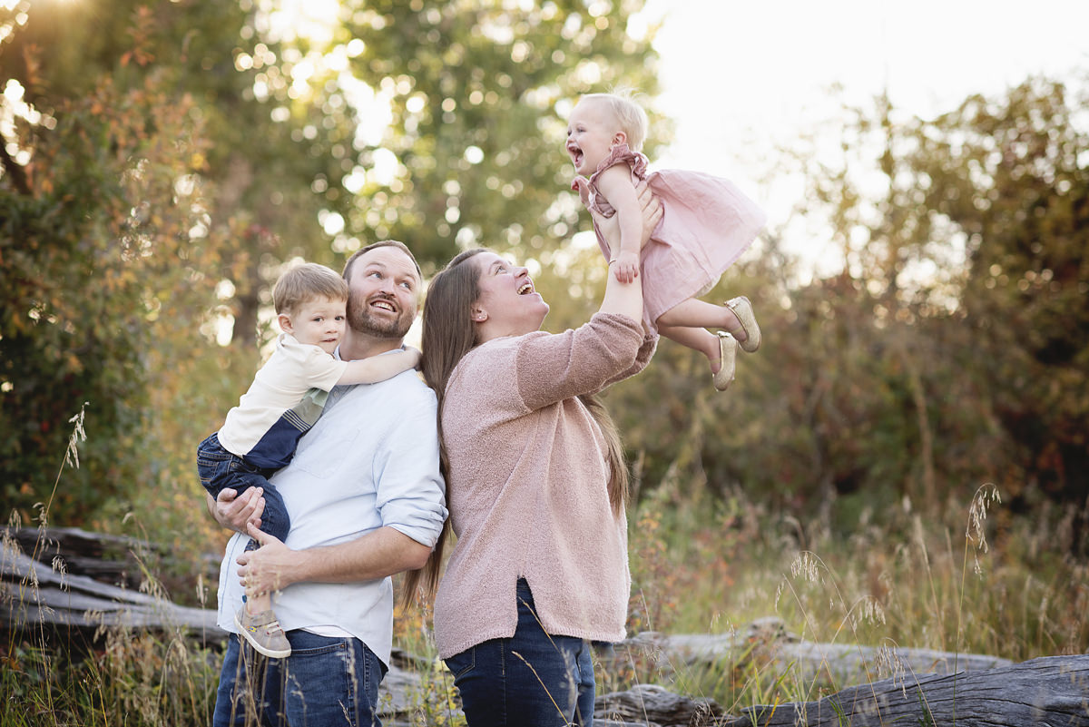Family with two kids, mom tossing little girl in the air, dad looking over his shoulder at the girl