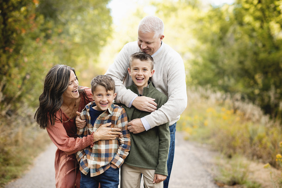 lifestyle professional family picture of kids smiling looking at the camera and mom and dad wrapping their arms around them