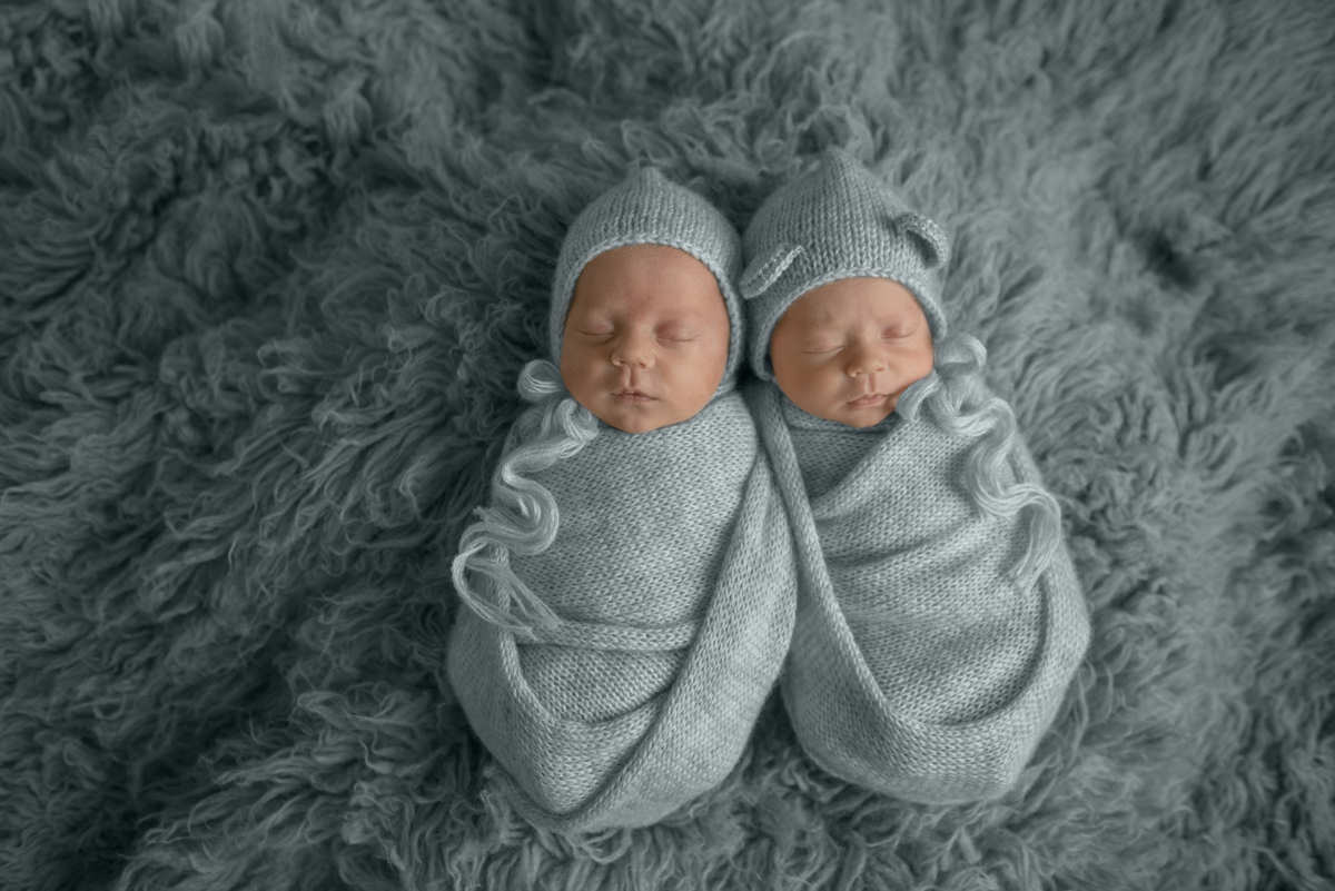 Twin Newborn babies wrapped in denim blue with baby bonnets laying in a blue flokati