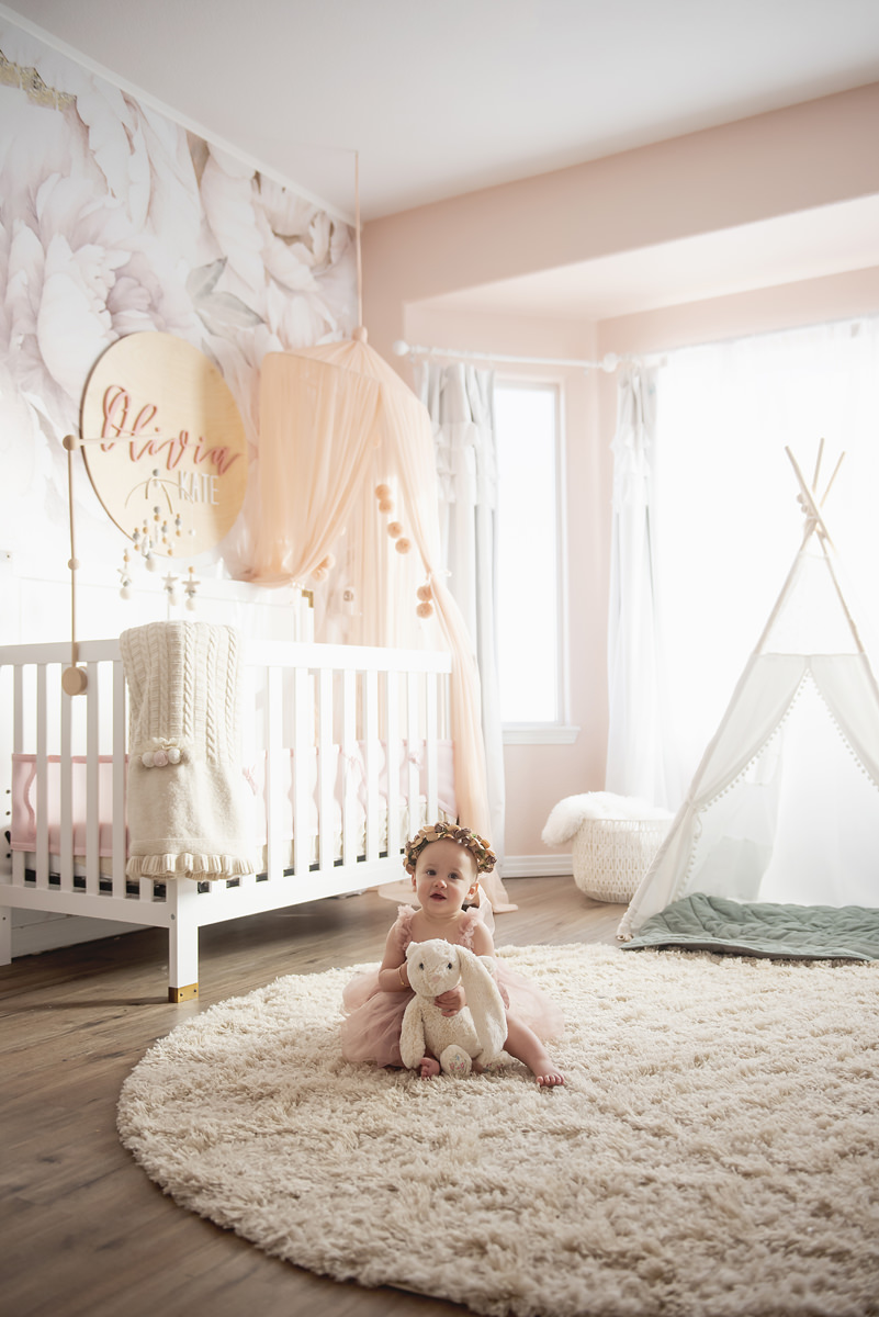 baby girl in her nursery professional photography boho style decor with pinks and green holding a bunny stuffed animal