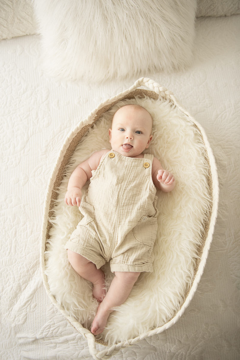 Five Month Old Baby in a Moses Basket Dressed in Neutral Creme colors laying down on a white bed spread