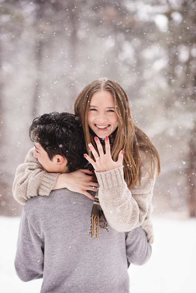 Snowy Engagement Pictures in Colorado Bride-to-be showing her engagement ring over guys shoulder