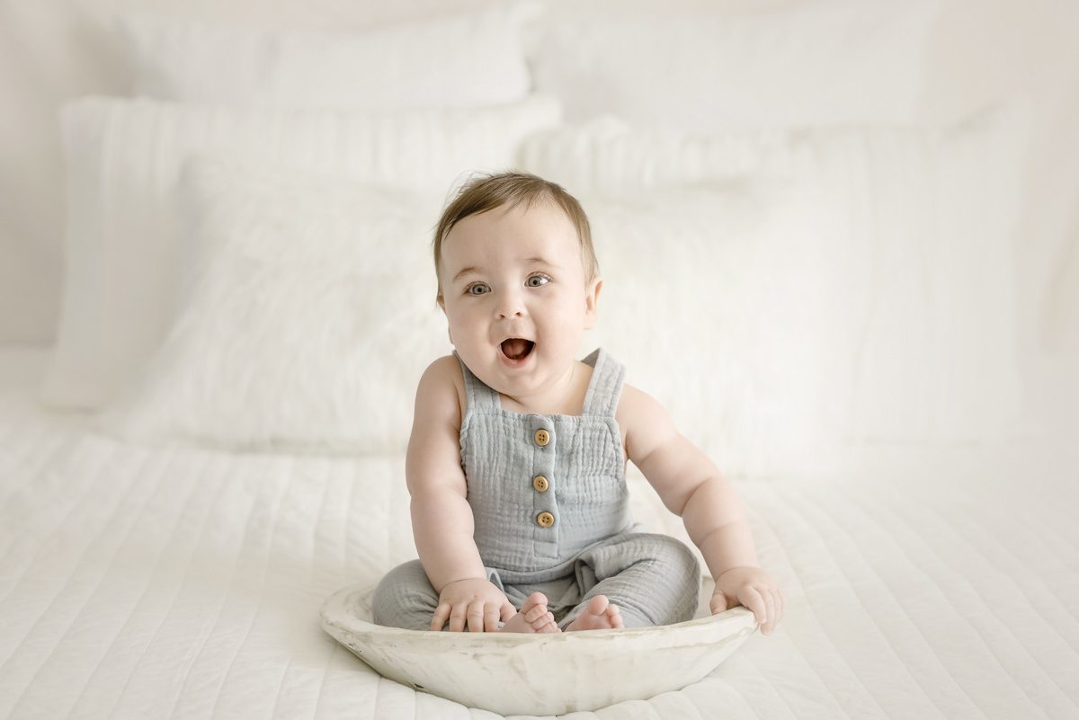 6 month baby in a bowl on a bed smiling