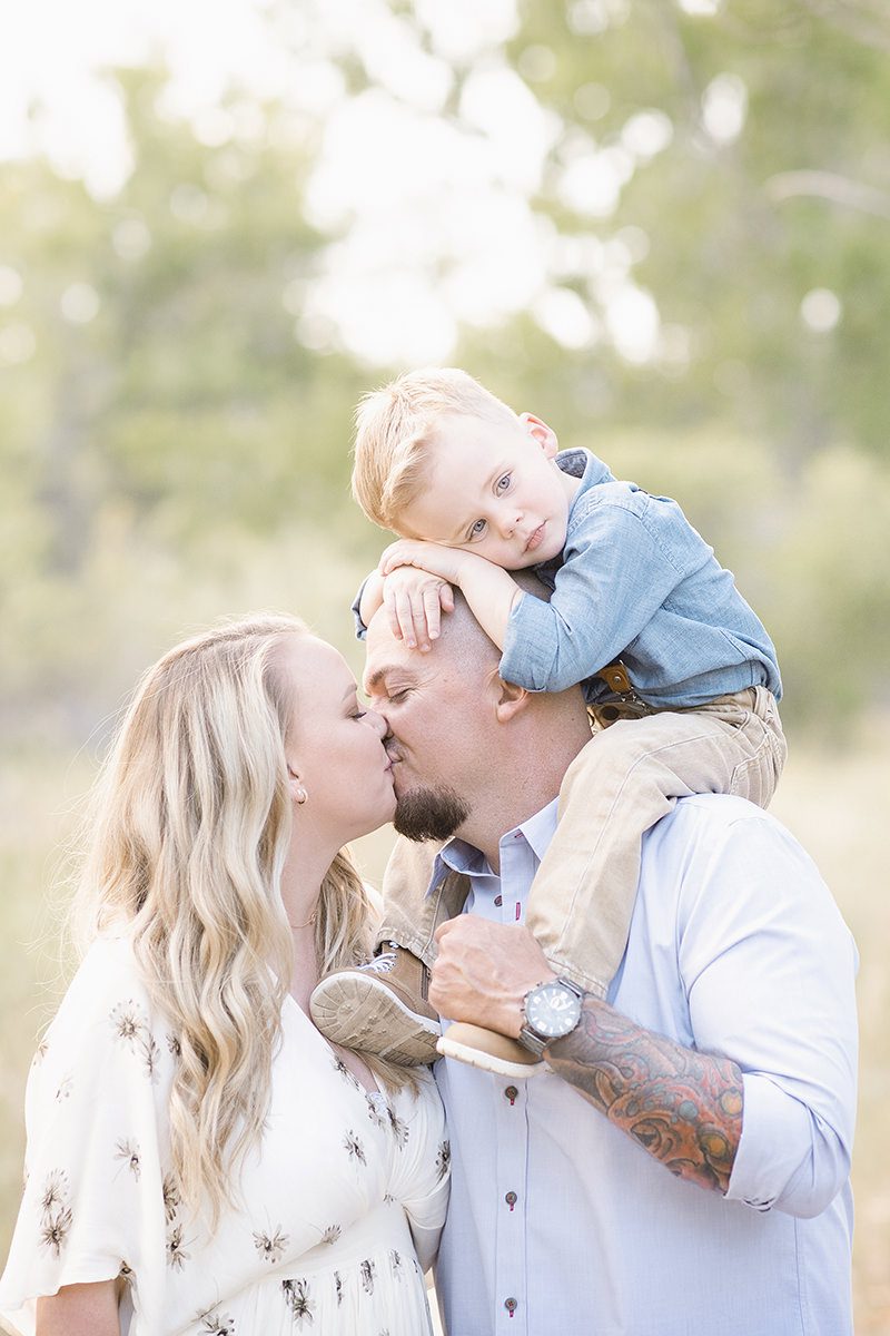 Mom and dad kissing with toddler on shoulders picture taken by Parker Family Photographer Jamie Herrera