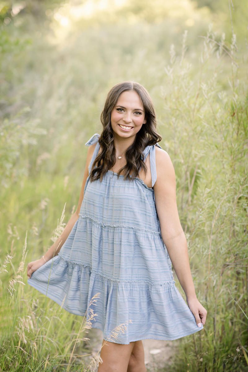 High school girl dressed in blue holding her skirt as if she's twirling for her Parker senior pictures