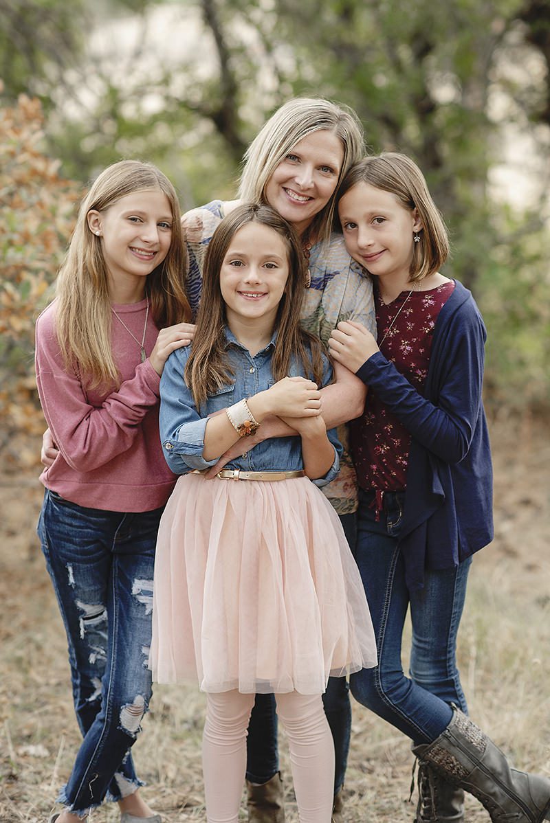 mom with her three daughters, snugged close and all looking at the camera, smiling