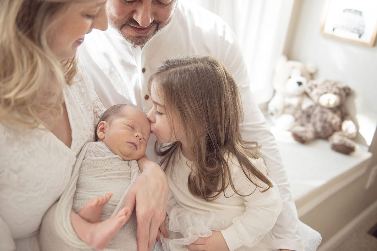 sister kissing newborn brother in nursery