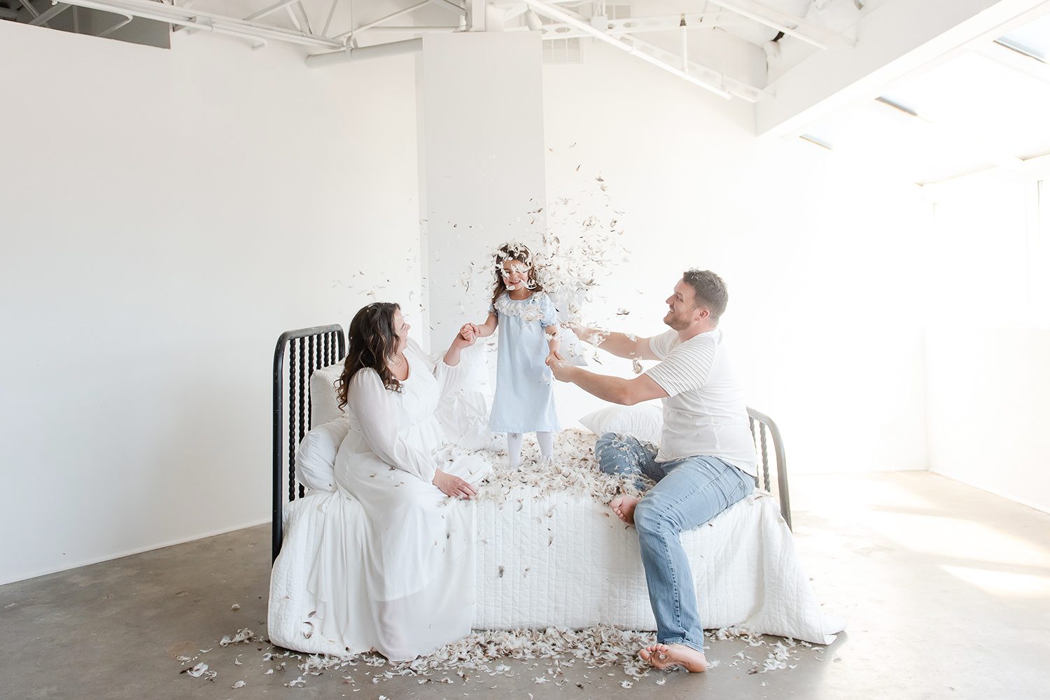 Family pillow fight on a bed with feathers in a white wall studio