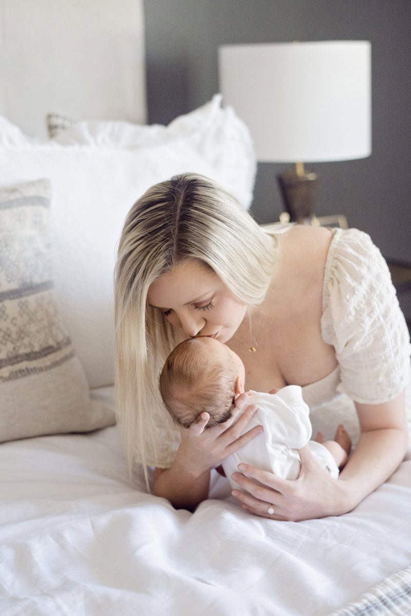 Mom leaning on bed kissing baby