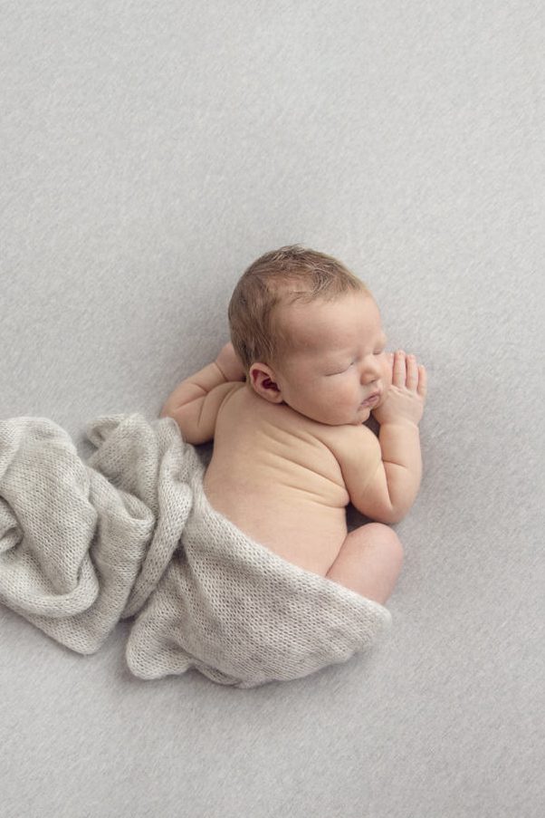 peacefully sleeping newborn curled on their side with a soft wrap draped around the body, neutral tones and gentle light