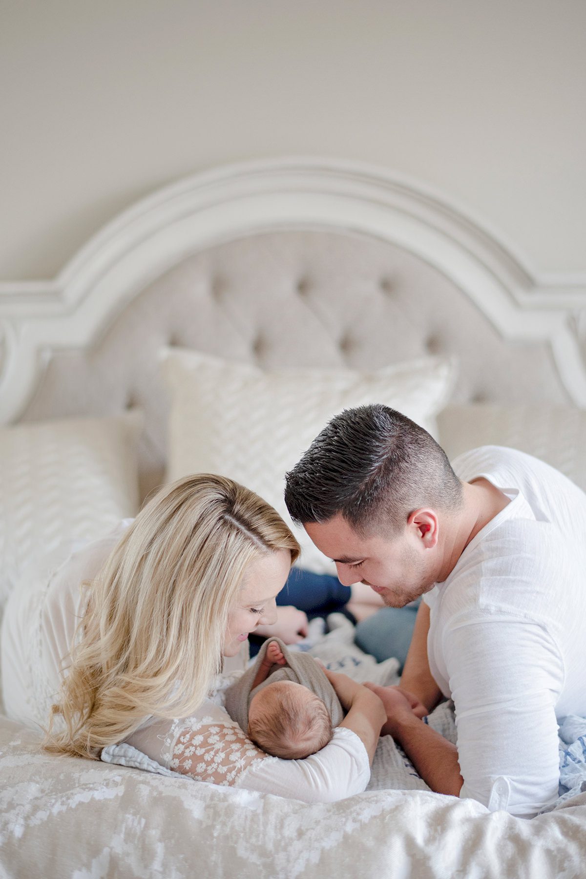 aurora newborn photographer capturing parents lying on a bed with their baby, soft natural light and intimate in-home lifestyle moment