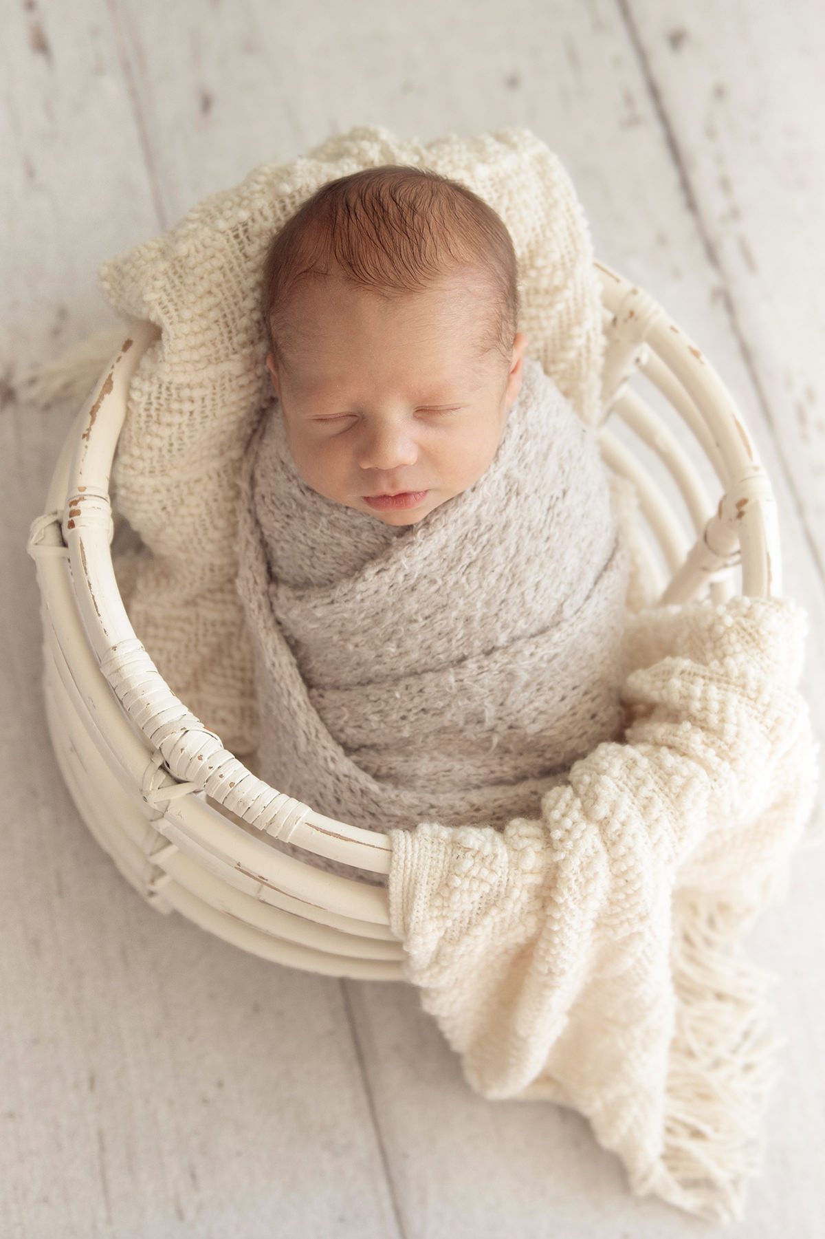 newborn photos of a peacefully sleeping baby wrapped in a soft knit blanket, resting in a white basket with neutral tones