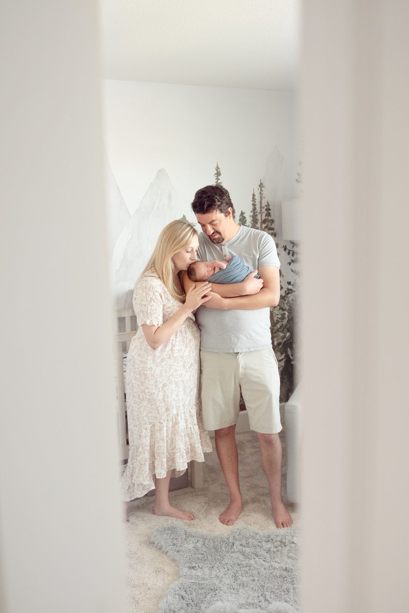 Mother kissing baby with dad in baby's nursery with the door slightly closed